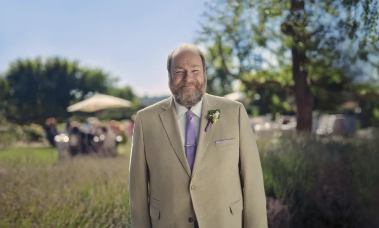 A man in a tan suit smiling at the camera